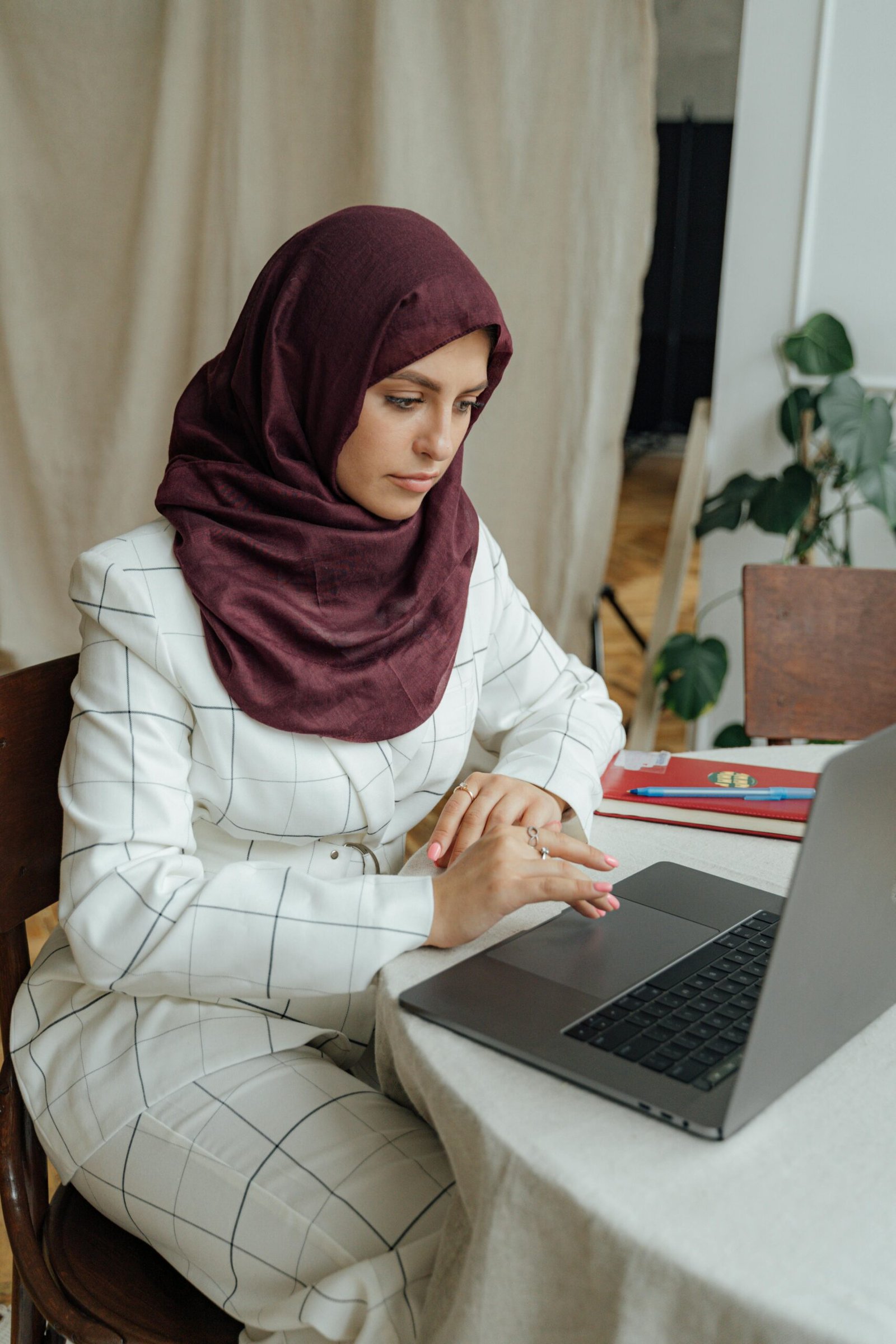 Businesswoman in hijab using a laptop in a home office setting.